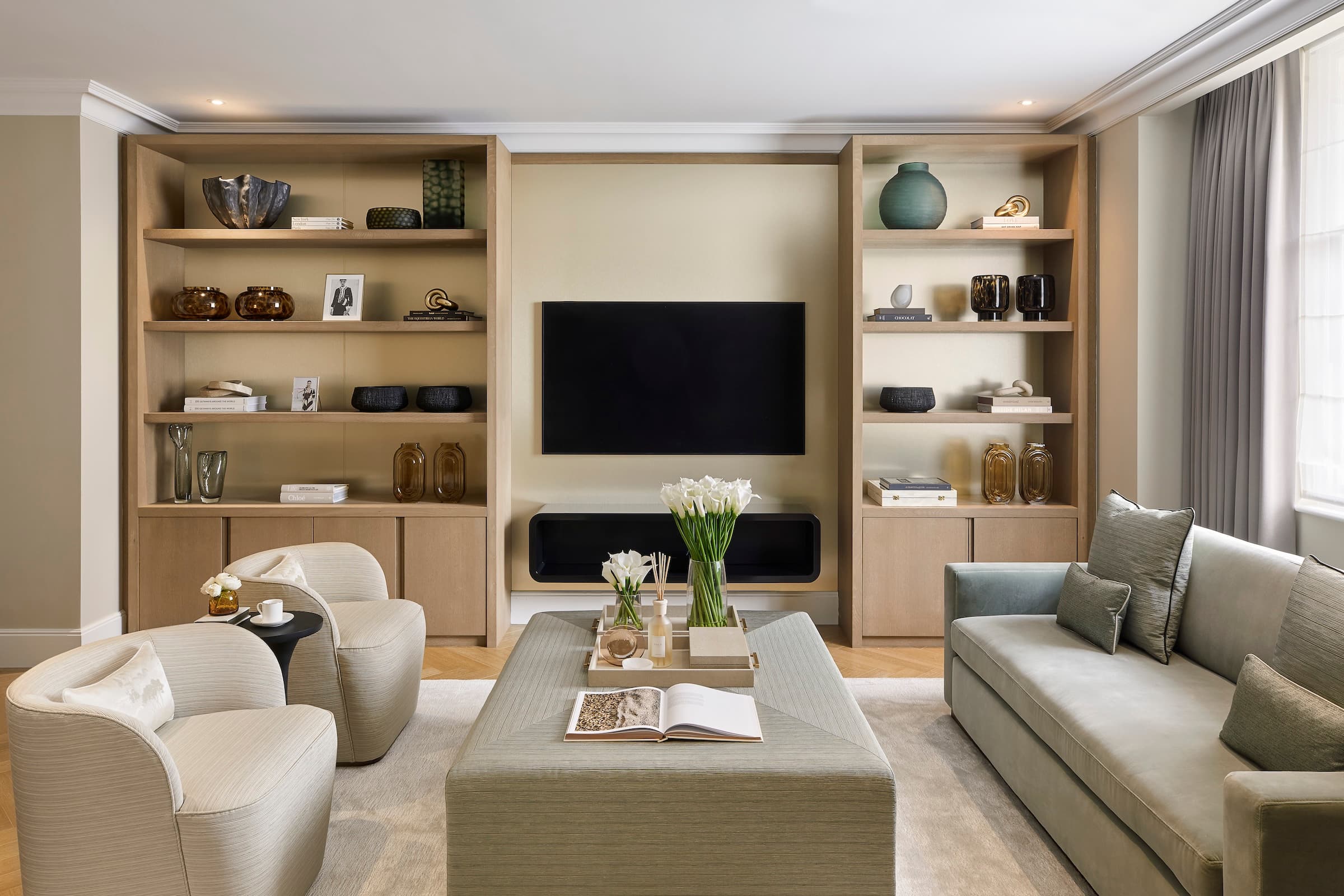 a living room with light wood shelving, a TV mounted on wall, floating shelf and sofas