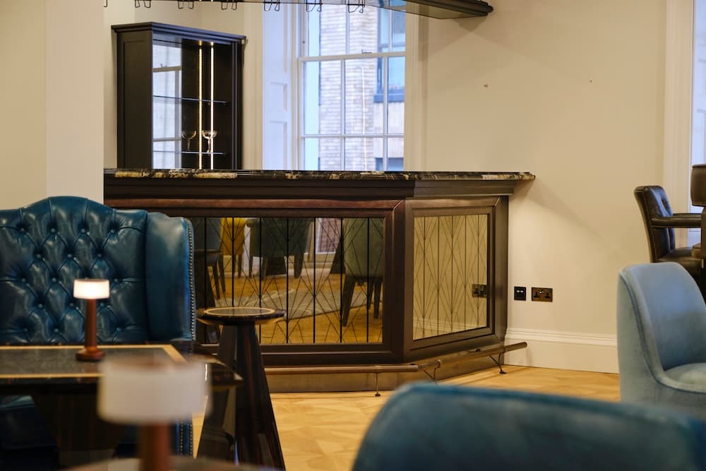 A sophisticated dark wood bar with a marble countertop, featuring custom-etched geometric glass panels and a brass footrail on light oak parquet flooring.