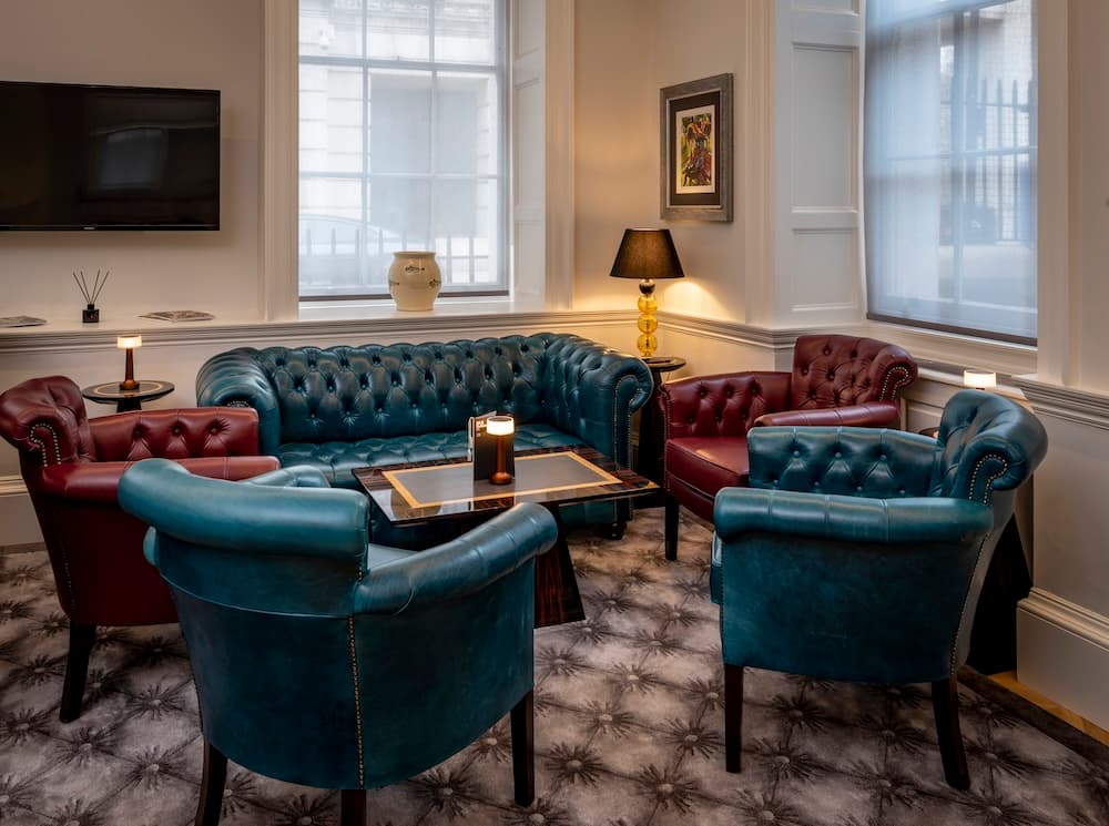Intimate seating area featuring a deep-buttoned teal leather Chesterfield sofa, matching burgundy wingback chairs, and warm, low-level designer table lamps.