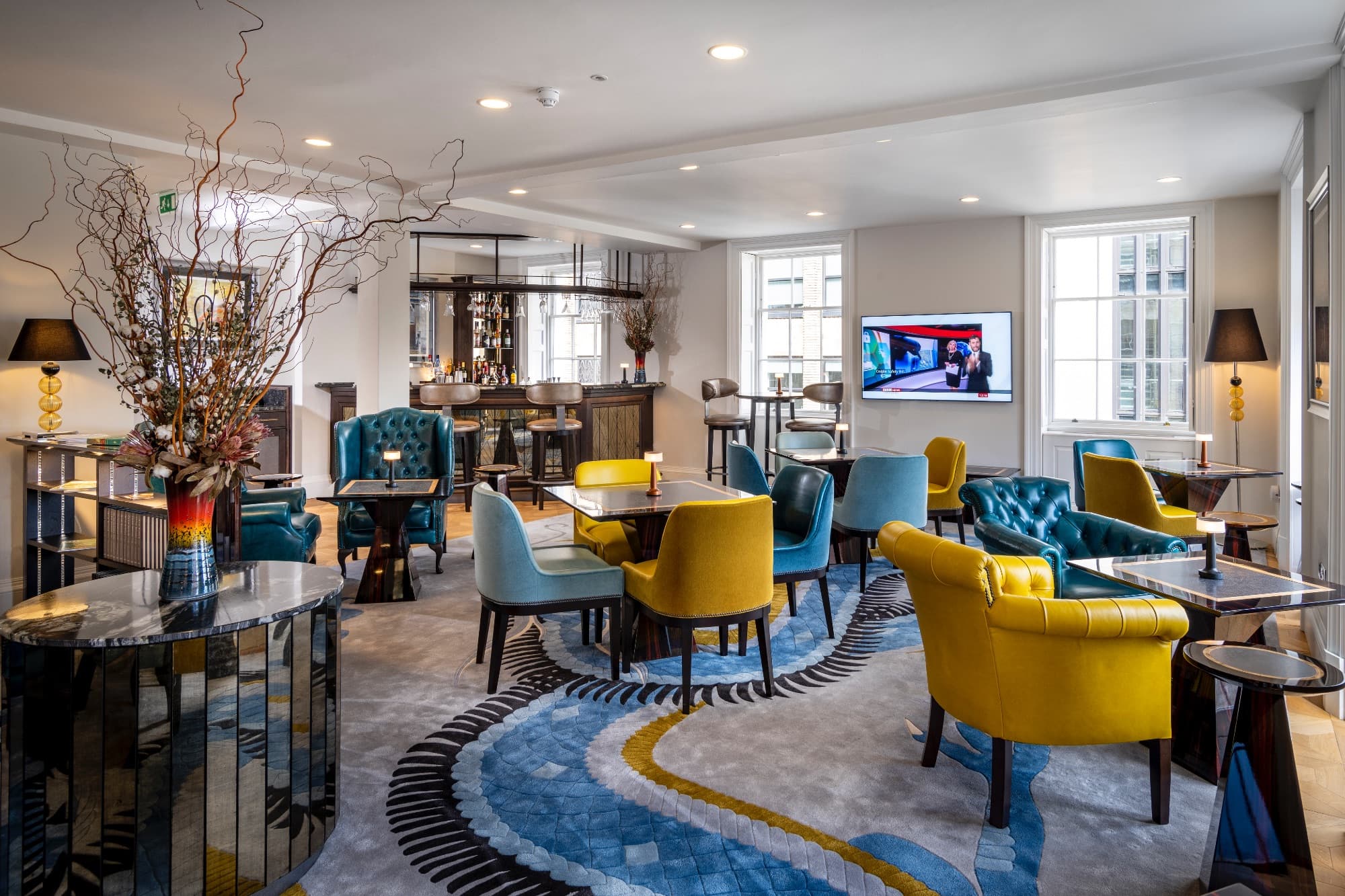 Wide view of the Robert Street Lounge featuring a historic marble fireplace, teal and burgundy leather seating, and a modern linear light fixture under an ornate period ceiling.
