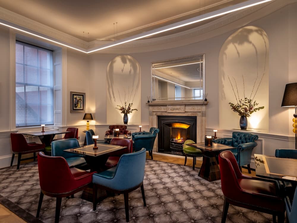 Intimate seating area featuring a deep-buttoned teal leather Chesterfield sofa, matching burgundy wingback chairs, and warm, low-level designer table lamps.